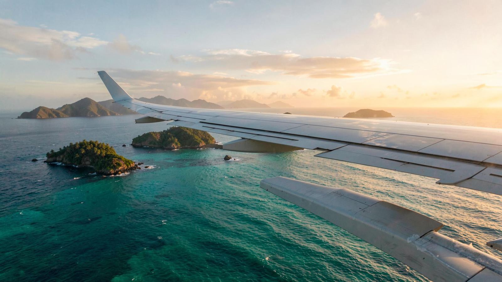 An aircraft wing above tropical islands at sunset